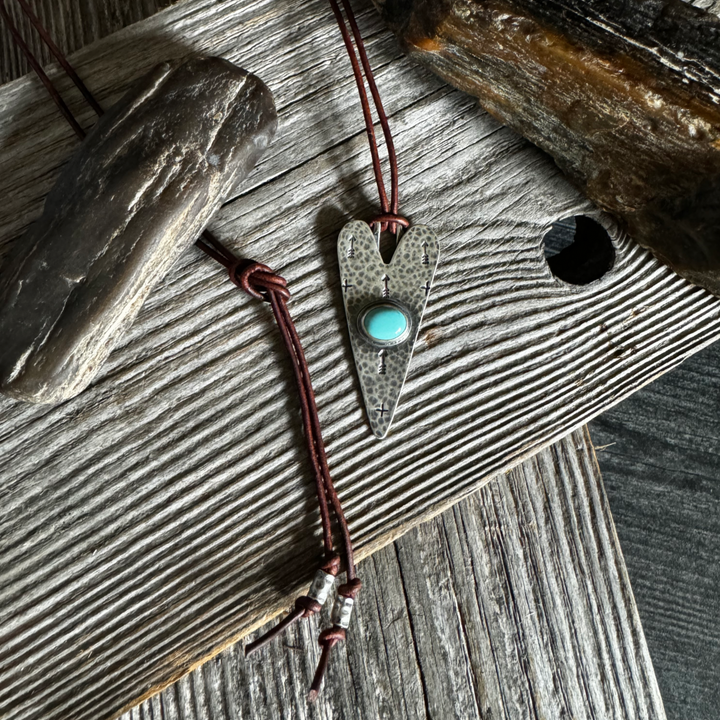 Handcrafted turquoise heart necklace with Carico Lake turquoise and sterling silver on a brown leather cord, styled on weathered wood with rustic stone accents.