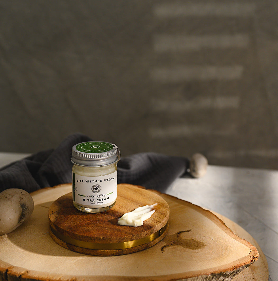 A small glass jar of Star Hitched Wagon Hazel Ultra Cream sits on a round wooden slice, with a dollop of ultra cream next to jar.
