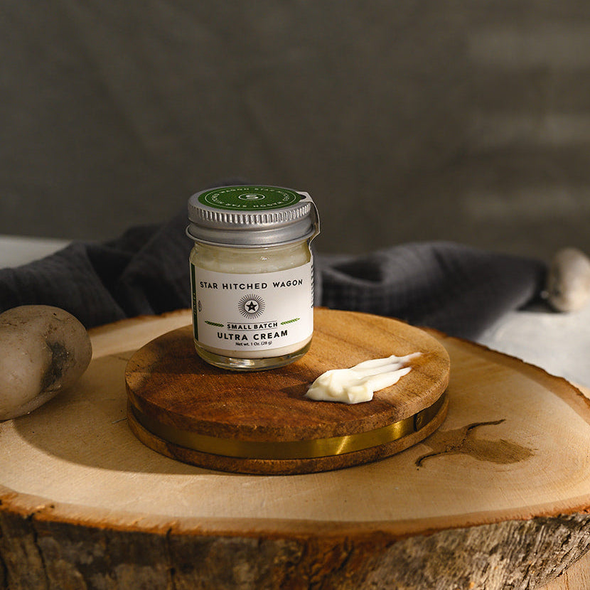 A small glass jar of Star Hitched Wagon Edie Ultra Cream sits on a round wooden slice, with a dollop of ultra cream next to jar.