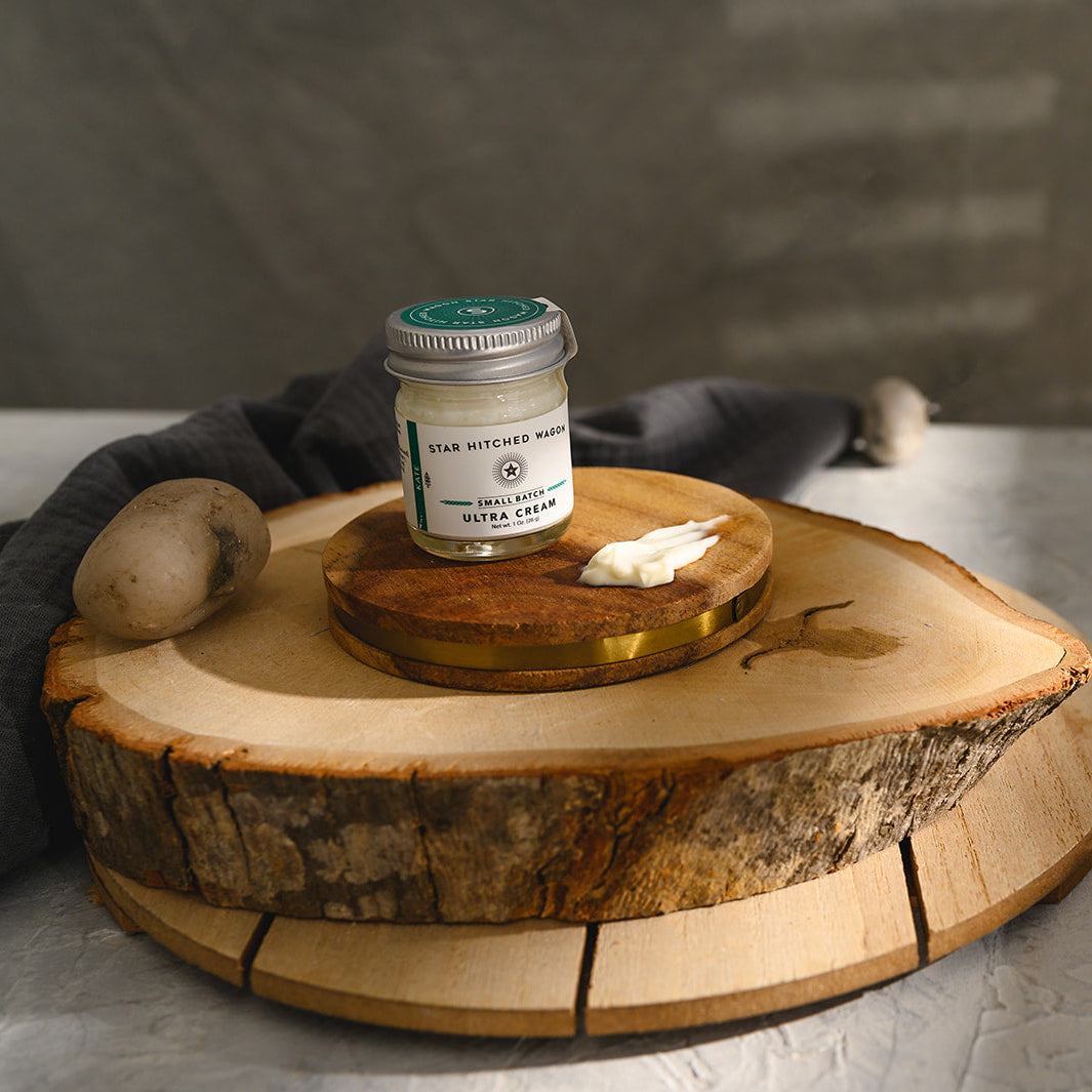 A small glass jar of Star Hitched Wagon Kate Ultra Cream sits on a round wooden slice, with a dollop of ultra cream next to jar.