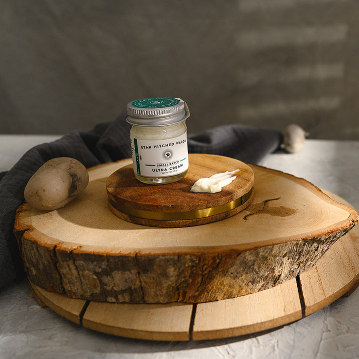 A small glass jar of Star Hitched Wagon Kate Ultra Cream sits on a round wooden slice, with a dollop of ultra cream next to jar.