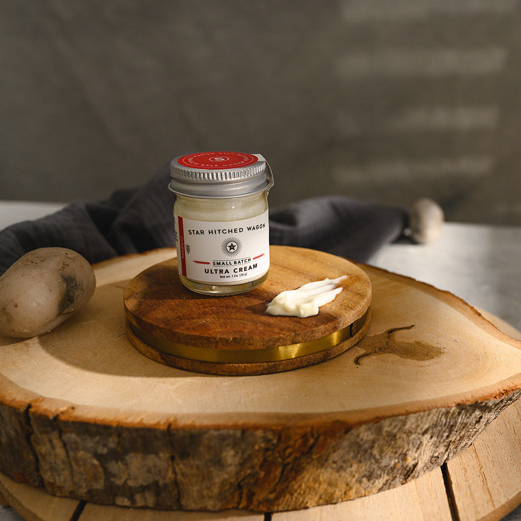 A small glass jar of Star Hitched Wagon Margo Ultra Cream sits on a round wooden slice, with a dollop of ultra cream next to jar.