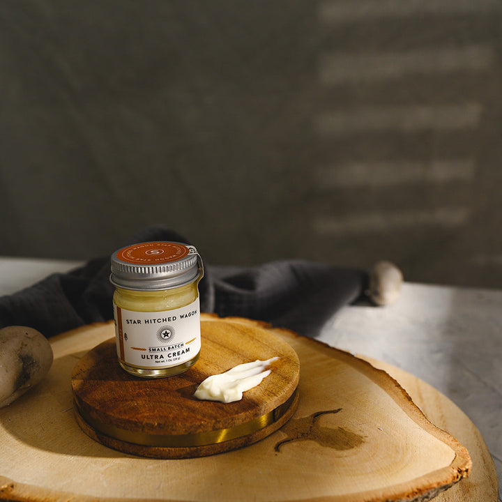 A small glass jar of Star Hitched Wagon Jess Ultra Cream sits on a round wooden slice, with a dollop of ultra cream next to jar.