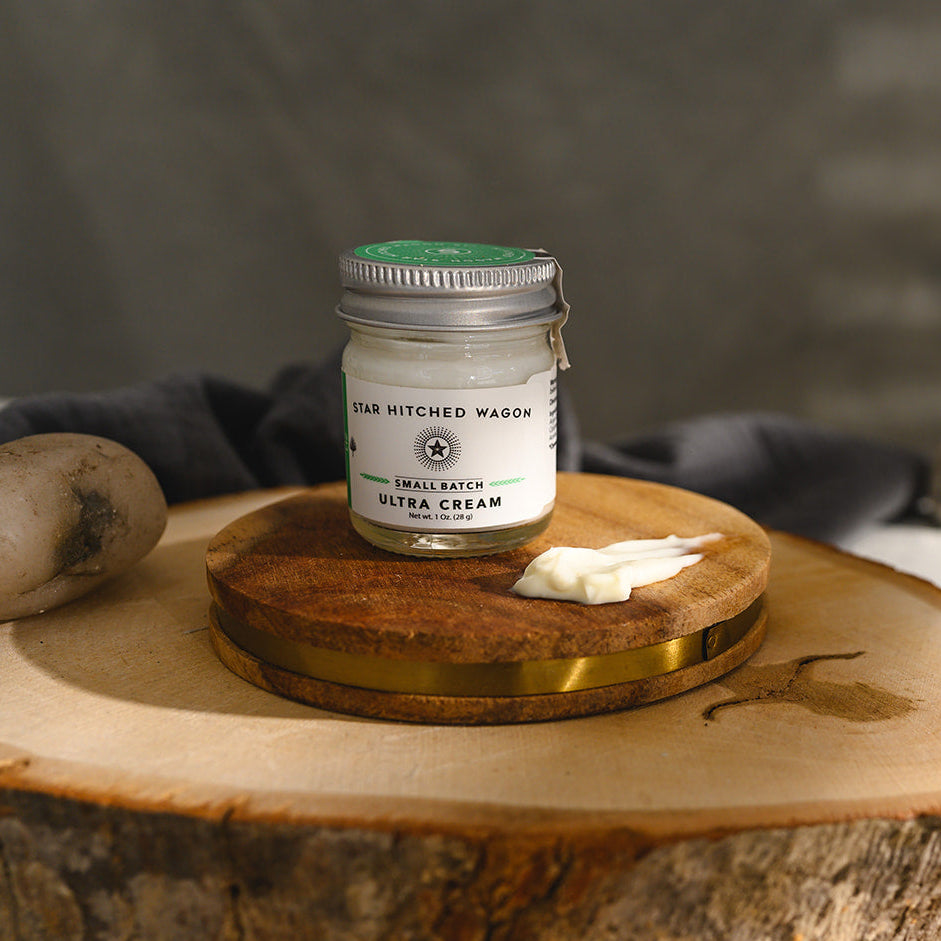 A small glass jar of Star Hitched Wagon Liz Ultra Cream sits on a round wooden slice, with a dollop of ultra cream next to jar.
