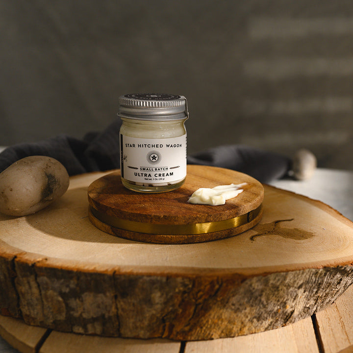 A small glass jar of Star Hitched Wagon Nora Ultra Cream sits on a round wooden slice, with a dollop of ultra cream next to jar.
