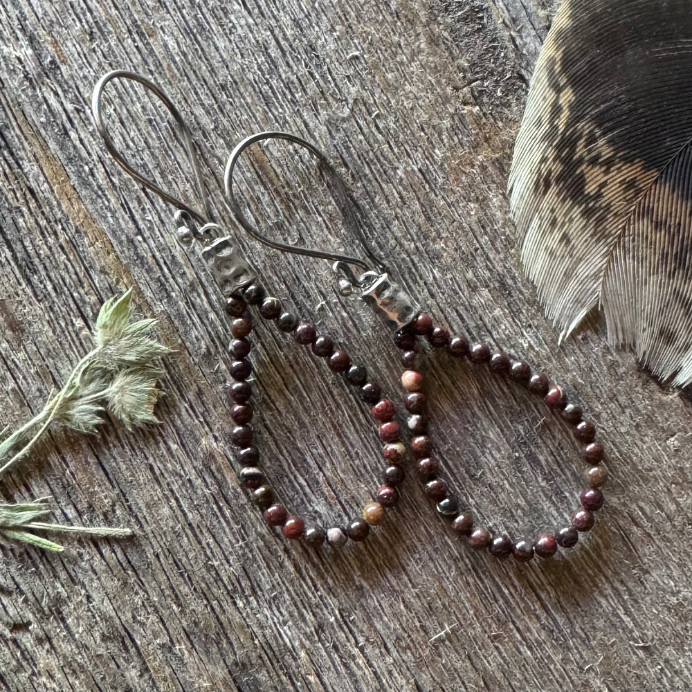 Jasper beaded earrings on a wooden surface with a feather and plant leaves.