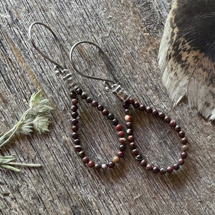Jasper beaded earrings on a wooden surface with a feather and plant leaves.