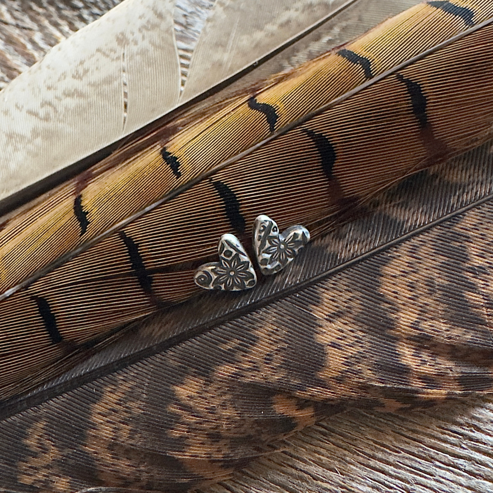 Small floral embossed sterling silver heart post earrings against a feather background.