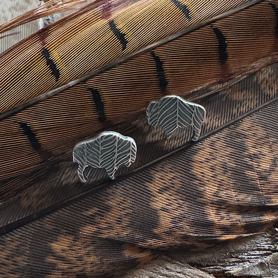 Silver buffalo post earrings with a feather texture on brown feather background