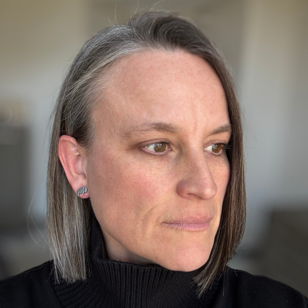 Woman with short hair wearing a black turtleneck sweater and sterling silver bison post earring against a blurred background.