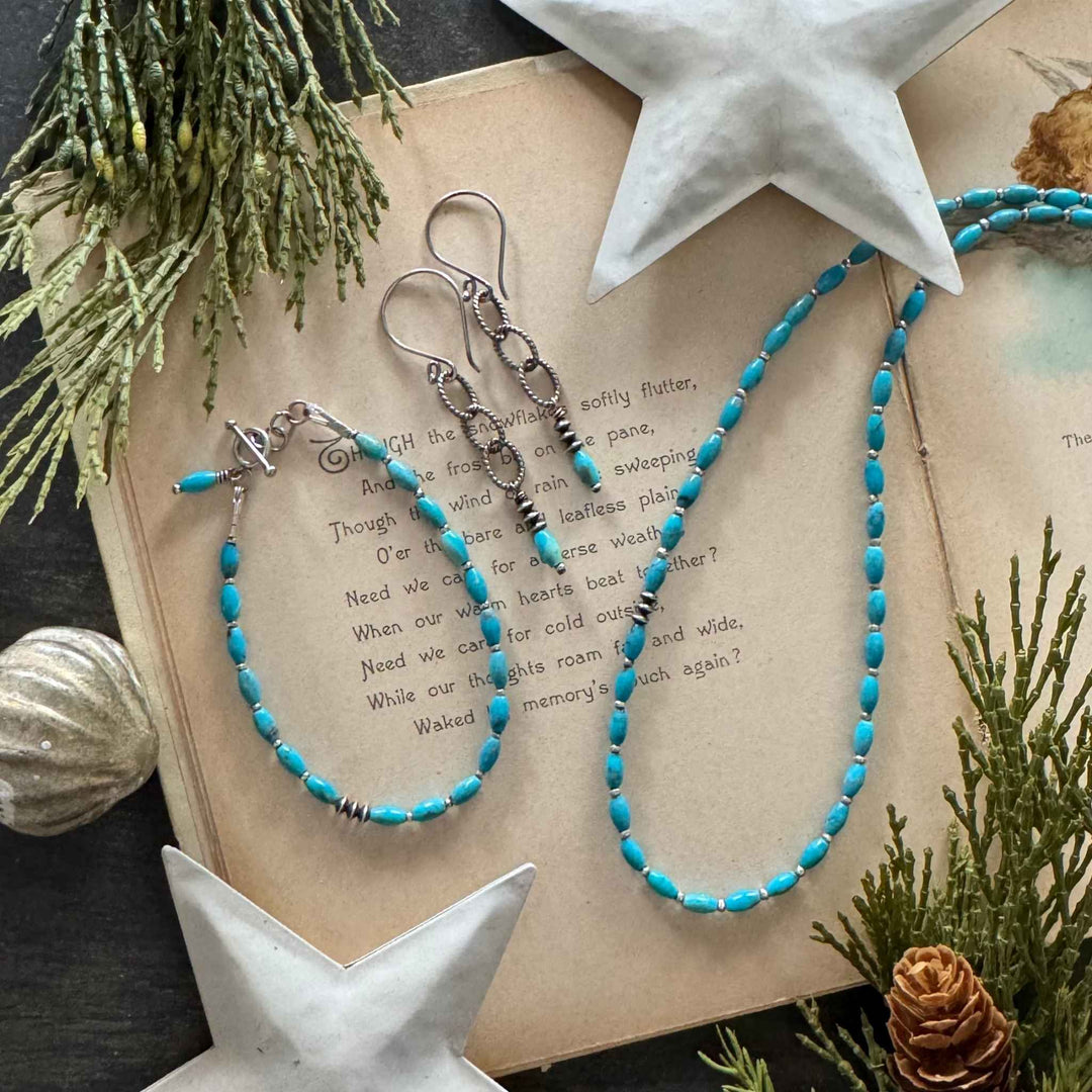 Bright Sky Turquoise necklace, bracelet, and chain-link earrings with oxidized silver accents displayed on a vintage holiday book with greenery and white stars.