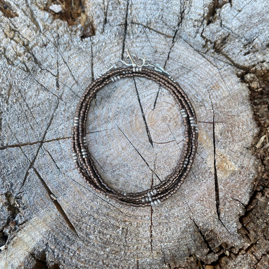 Matte brown seed bead wrap bracelet with Thai silver rondelles and a Bali silver toggle clasp displayed coiled on a stone background.
