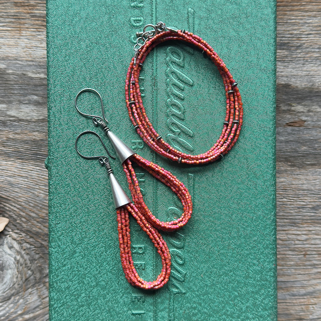 Bright coral pink seed bead earrings and wrap bracelet on green metal background.