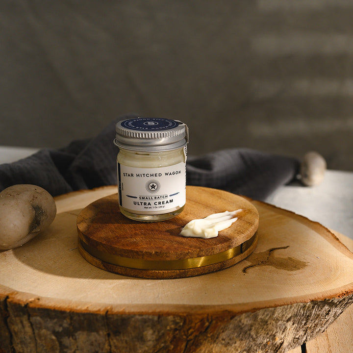 A small glass jar of Star Hitched Wagon Edie Ultra Cream sits on a round wooden slice, with a dollop of ultra cream next to jar.