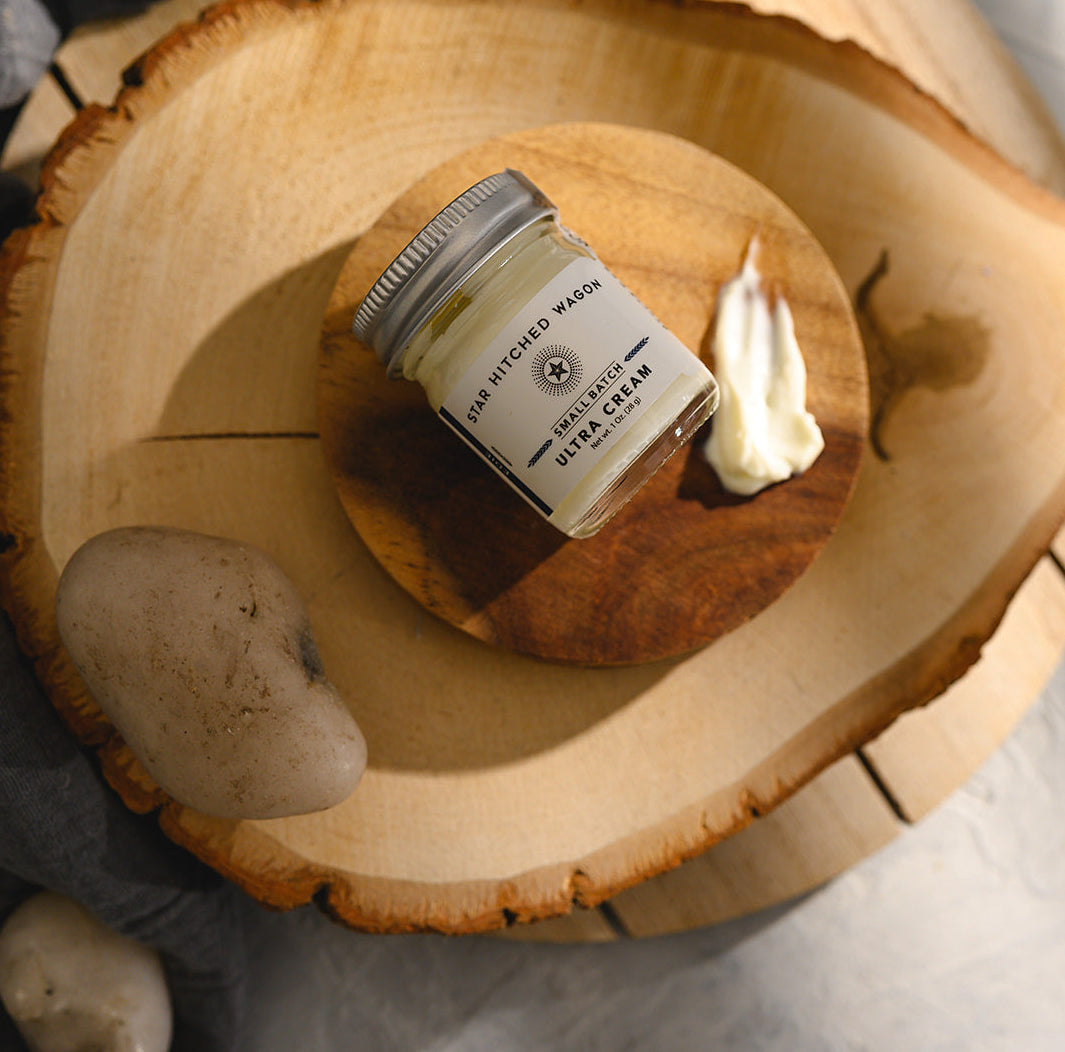 A small glass jar of Star Hitched Wagon Edie Ultra Cream lays on a round wooden slice, with a dollop of ultra cream next to jar.