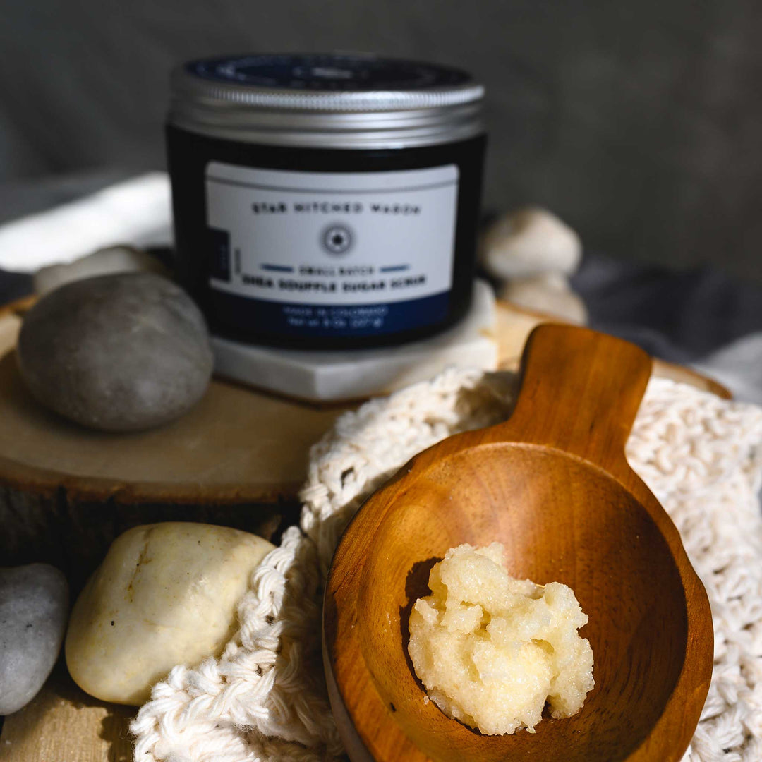 A close up of Edie Shea Souffle Sugar Scrub displayed in a wooden surface, accompanied by the full jar of scrub and a knit wash cloth.