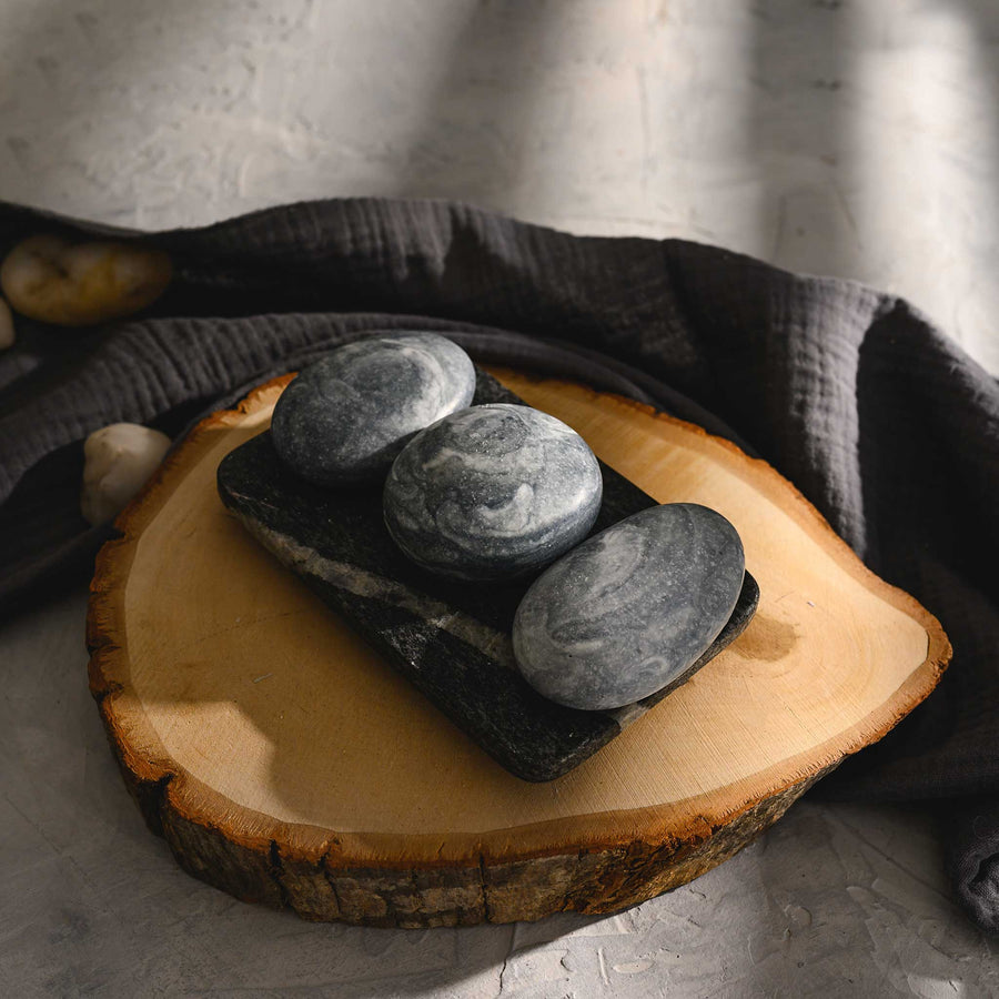 Edie river stone salt soap trio displayed on a wooden slice, with a dark cloth backdrop.