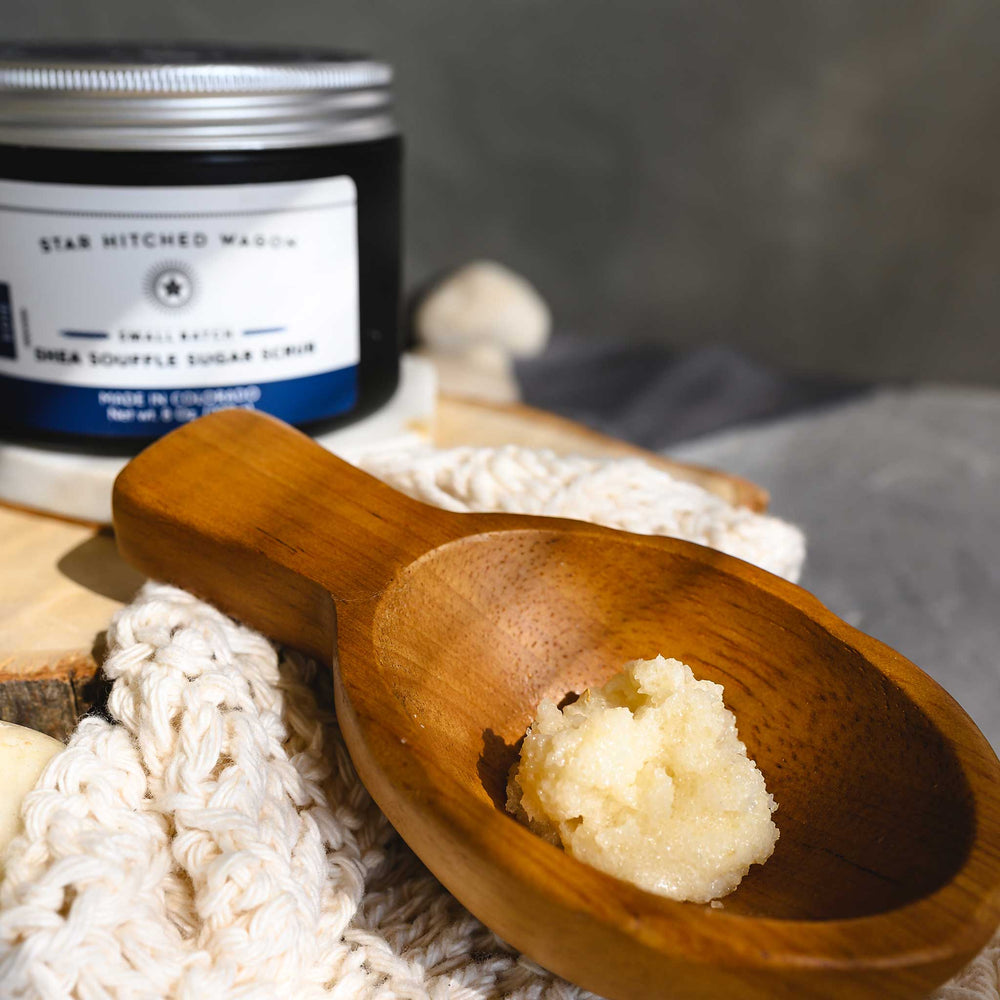 A close up of Edie Shea Souffle Sugar Scrub displayed in a wooden surface, accompanied by the full jar of scrub and a knit wash cloth.