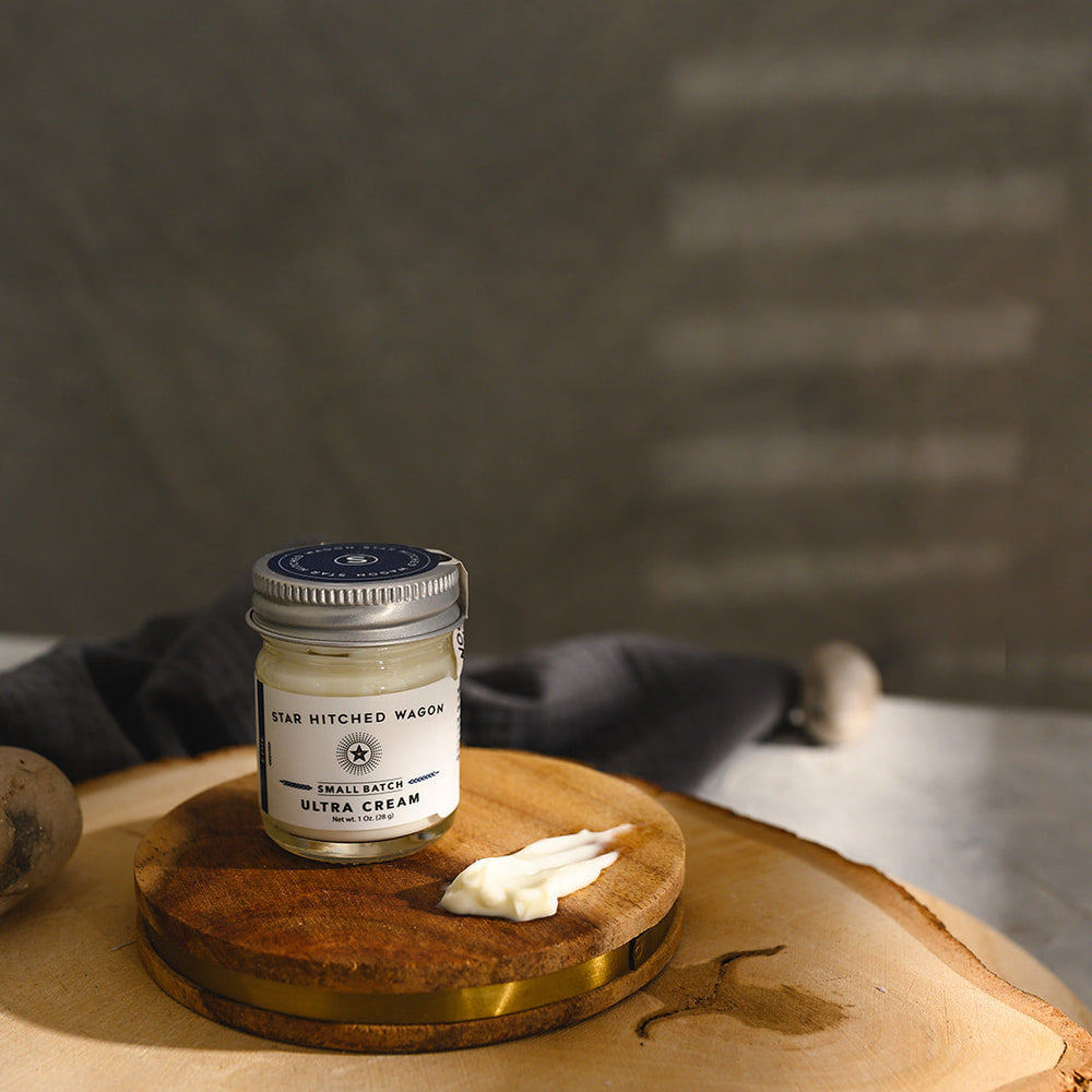 A small glass jar of Star Hitched Wagon Edie Ultra Cream sits on a round wooden slice, with a dollop of ultra cream next to jar.