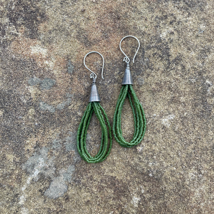 Green seed bead earrings with sterling silver ear wires and Bali-style cone tops displayed on a textured stone background.