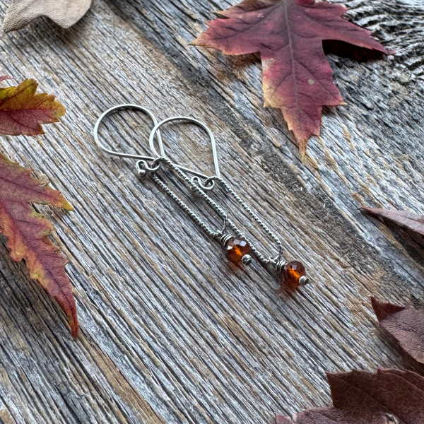 Harvest Glow -  Spessartite Garnet and Silver Earring surrounded by fall leaves on wooden backdrop