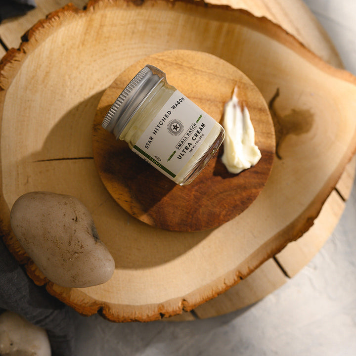 A small glass jar of Star Hitched Wagon Hazel Ultra Cream lays on a round wooden slice, with a dollop of ultra cream next to jar.