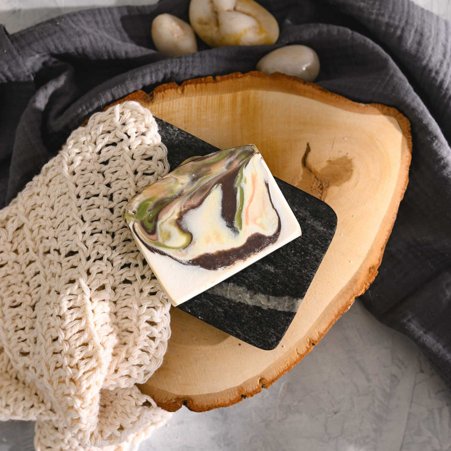Hazel essential oil soap bar with swirls of peach, green, brown, and cream, placed on a wooden surface with a knit washcloth beside it.