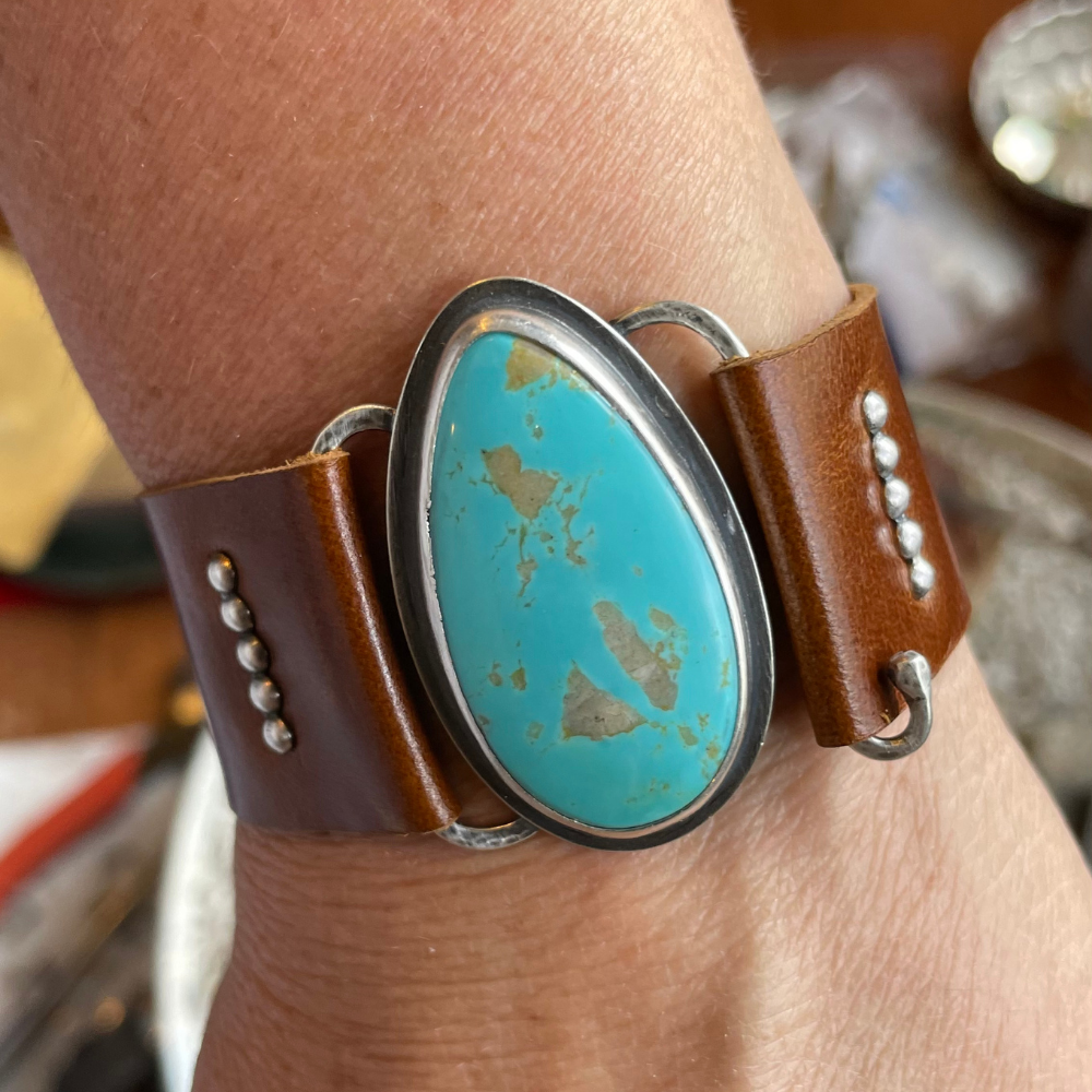 Brown leather bracelet with a turquoise stone on a wrist.