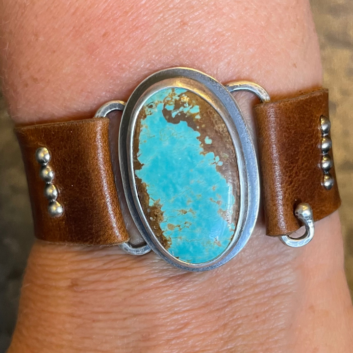 Brown leather cuff with turquoise stone and silver accents on a wrist.