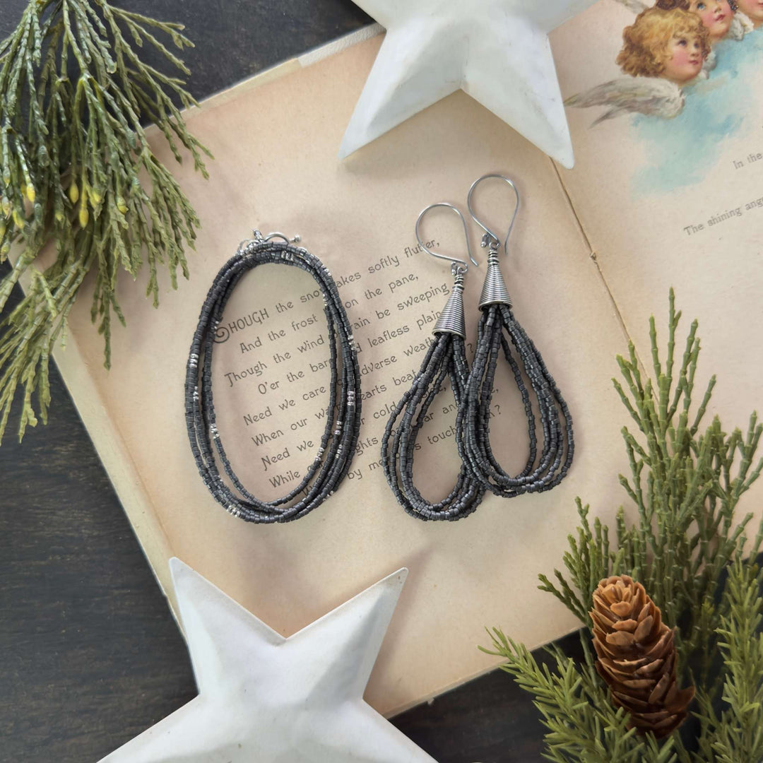 Dark grey metallic seed bead wrap bracelet and matching multi-loop earrings with Bali cones displayed on an open vintage holiday book with greenery and stars.