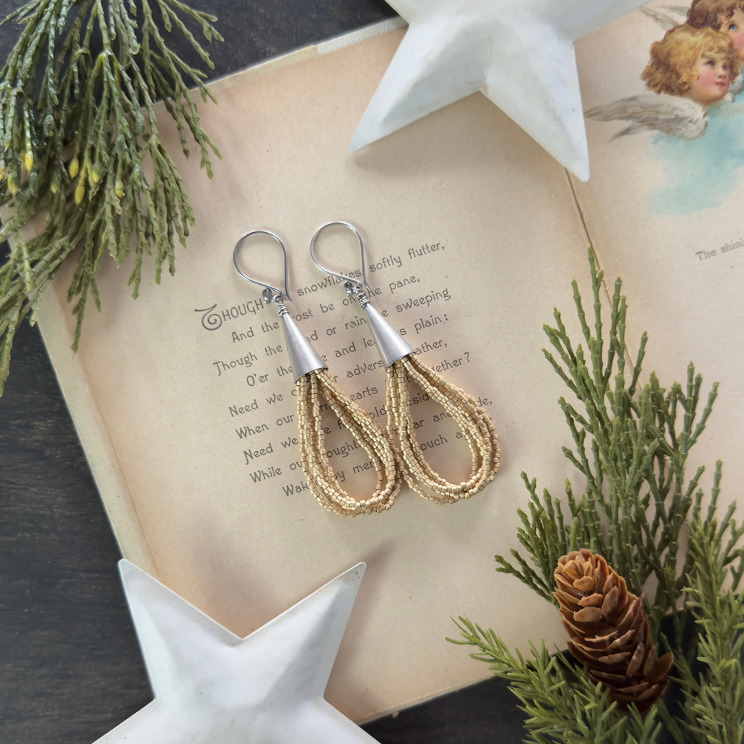 Matte gold multi-loop beaded earrings with smooth Bali cones displayed on an open vintage holiday book with greenery and white star decor.
