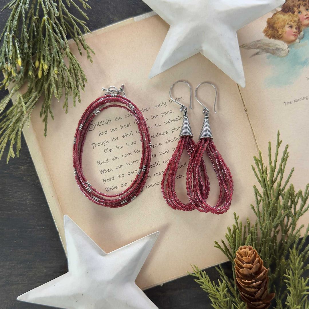 Satin Cranberry metallic seed bead wrap bracelet and matching loop earrings with Bali cones on a vintage holiday book with greenery and white stars.