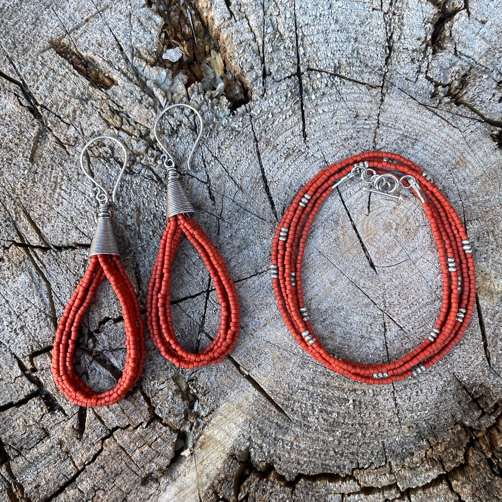 Matte orange seed bead earrings and wrap bracelet on a textured wooden background.