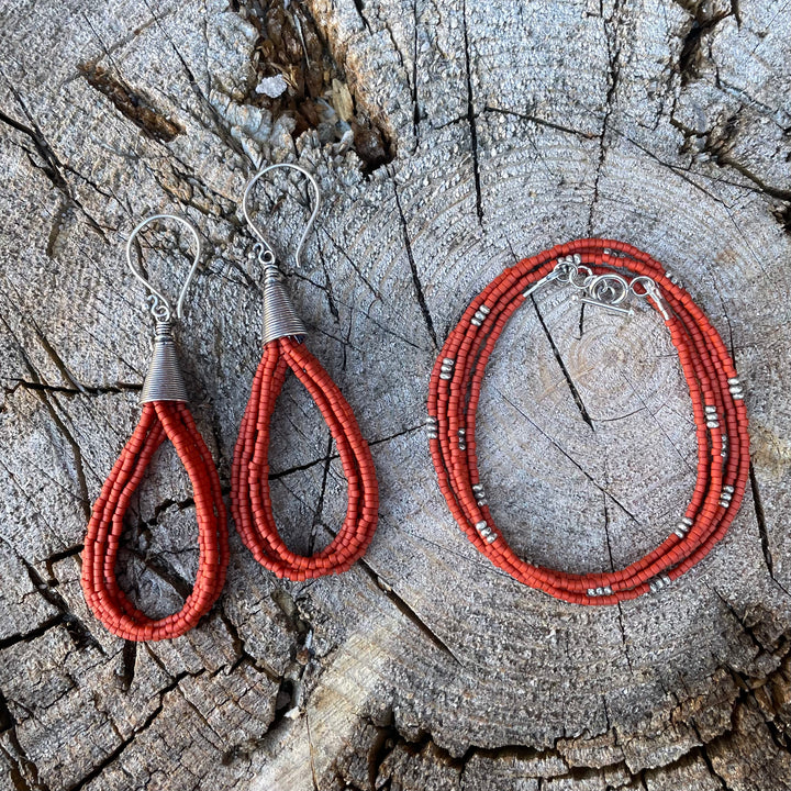Matte orange seed bead earrings and wrap bracelet on a textured wooden background.