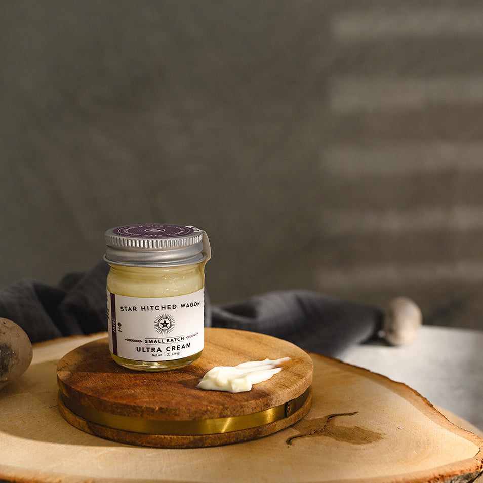 A small glass jar of Star Hitched Wagon Jane Ultra Cream sits on a round wooden slice, with a dollop of ultra cream next to jar.
