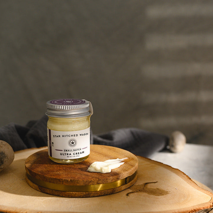 A small glass jar of Star Hitched Wagon Jane Ultra Cream sits on a round wooden slice, with a dollop of ultra cream next to jar.