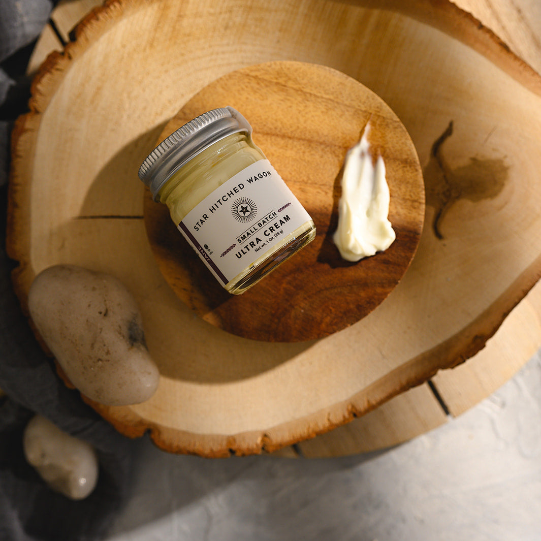 A small glass jar of Star Hitched Wagon Jane Ultra Cream lays on a round wooden slice, with a dollop of ultra cream next to jar.