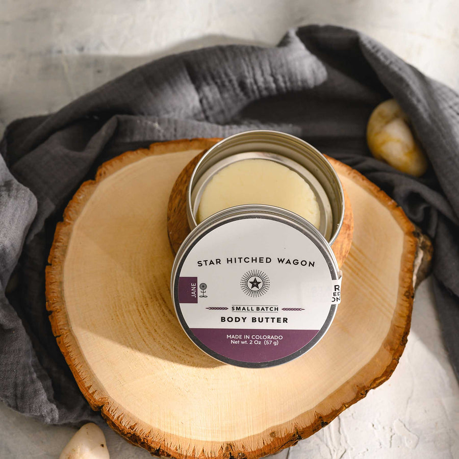 Jane 2 Ounce Body Butter Moisturizer Bar in reusable tin on wood slice.