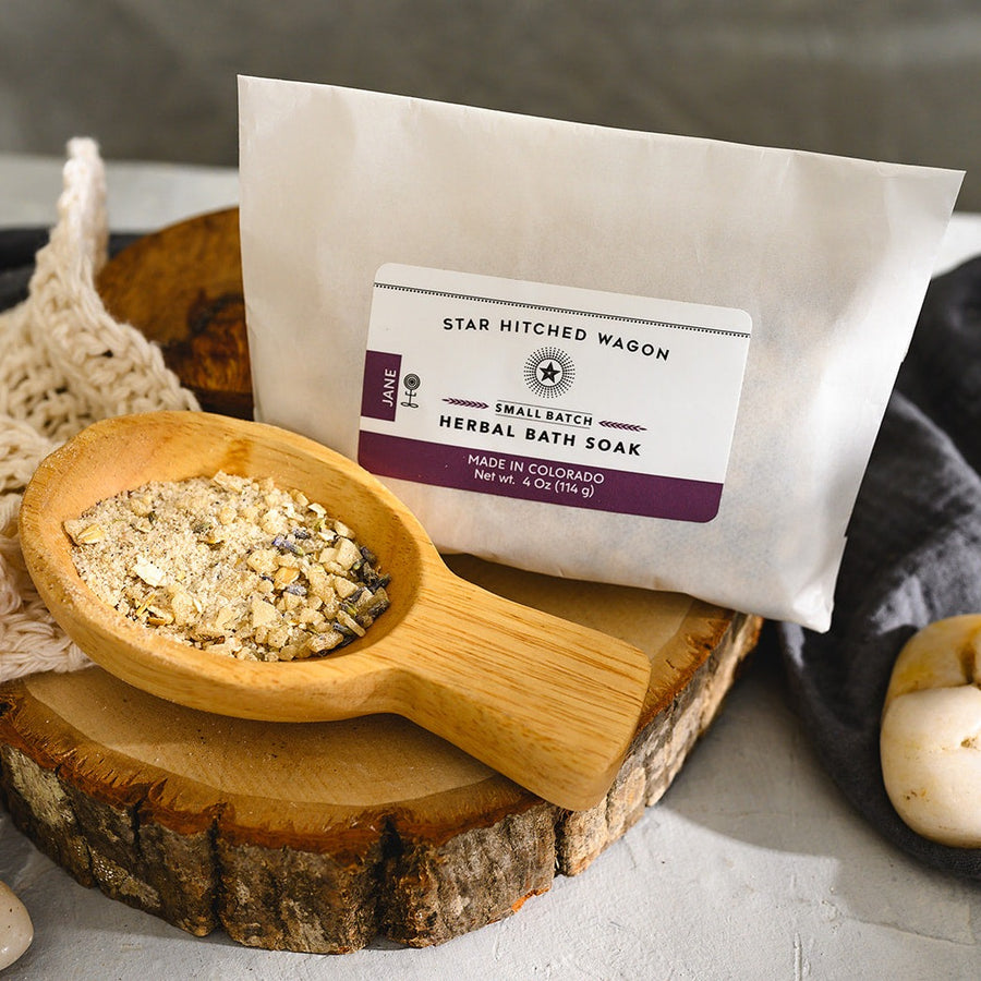 Jane herbal bath soak individual pouch next to wooden spoon with some of soka in spoon.