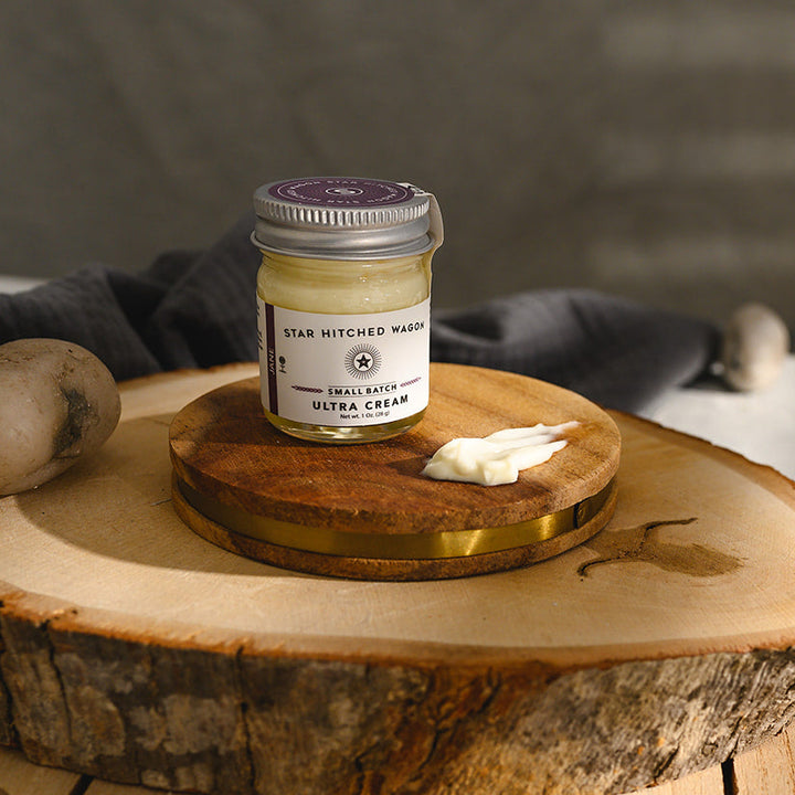 A small glass jar of Star Hitched Wagon Jane Ultra Cream sits on a round wooden slice, with a dollop of ultra cream next to jar.
