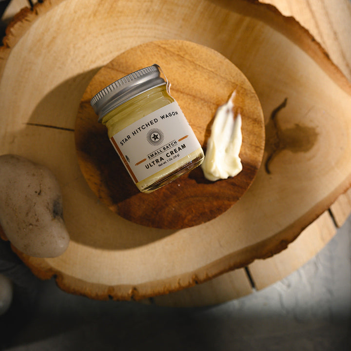 A small glass jar of Star Hitched Wagon Jess Ultra Cream lays on a round wooden slice, with a dollop of ultra cream next to jar.