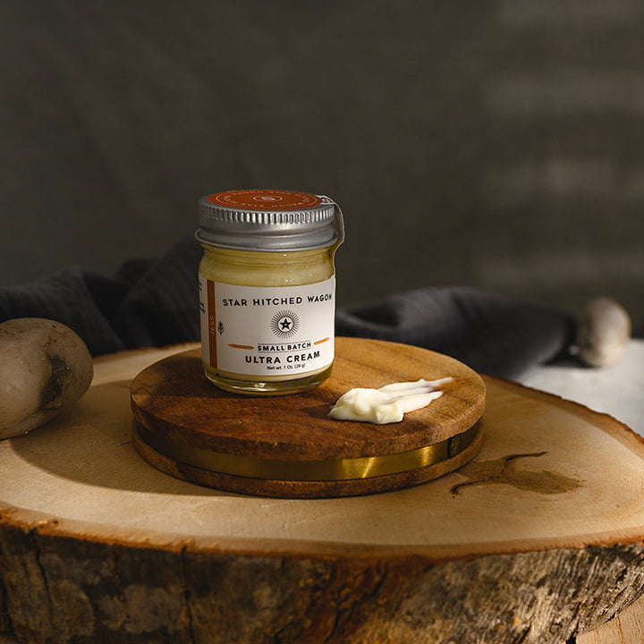 A small glass jar of Star Hitched Wagon Jess Ultra Cream sits on a round wooden slice, with a dollop of ultra cream next to jar.