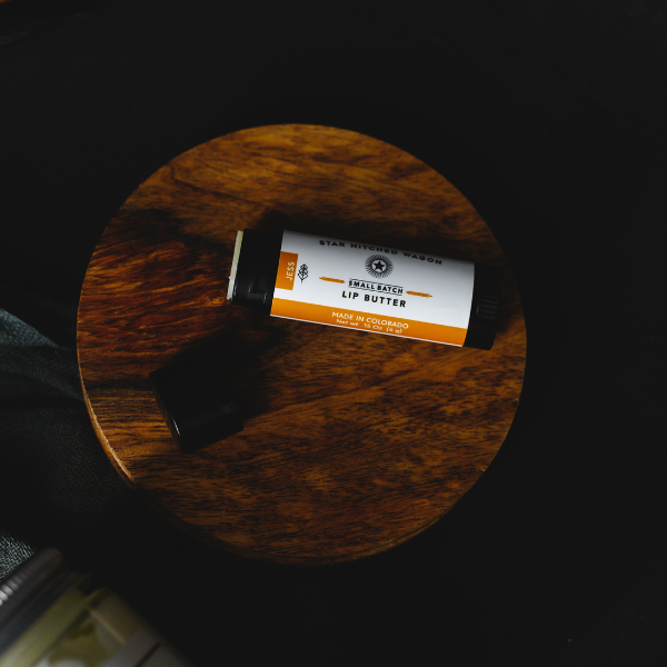 An opened tube of Jess lip butter on a wooden surface with a dark background