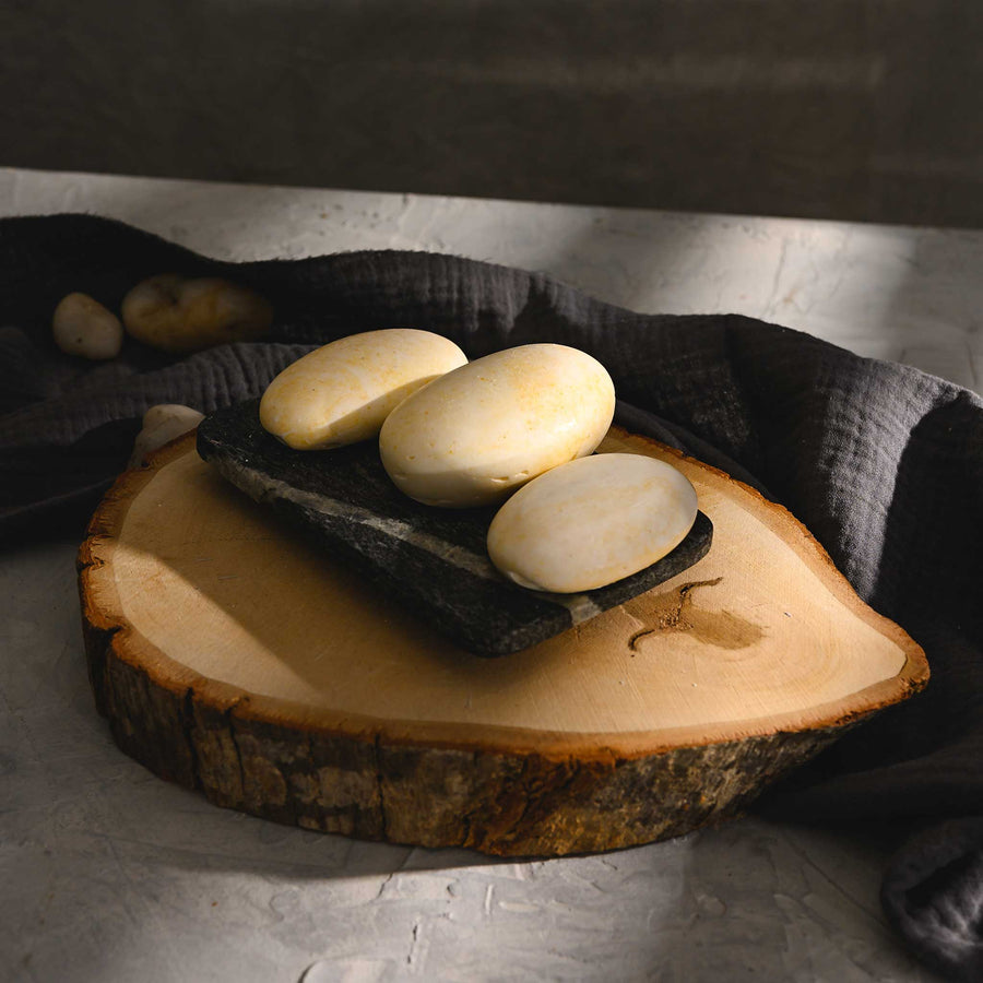 Jess river stone salt soap trip, placed on a wooden disc with a dark cloth background.