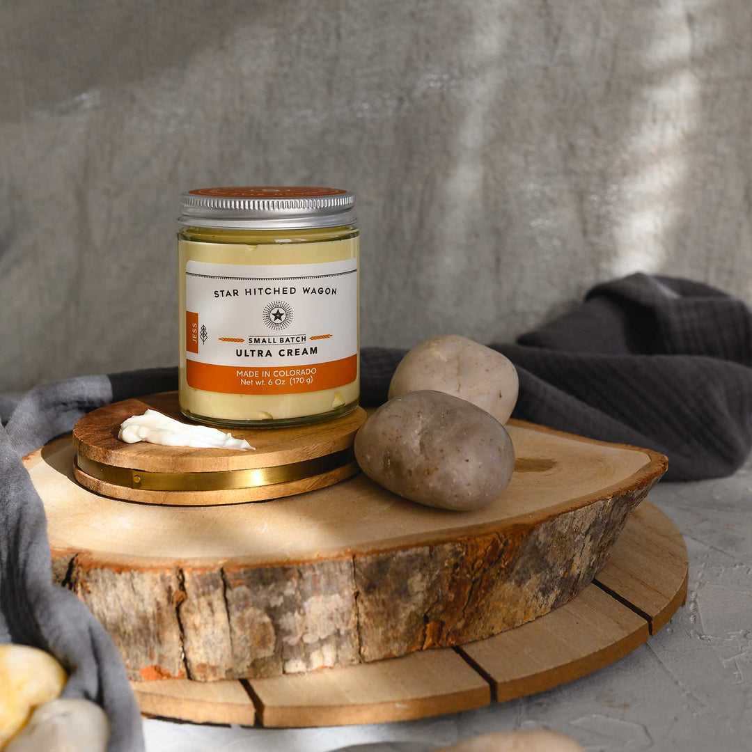Jess Ultra Cream in a glass jar placed on a wooden platform, pebbles and grey towel in foreground and background.