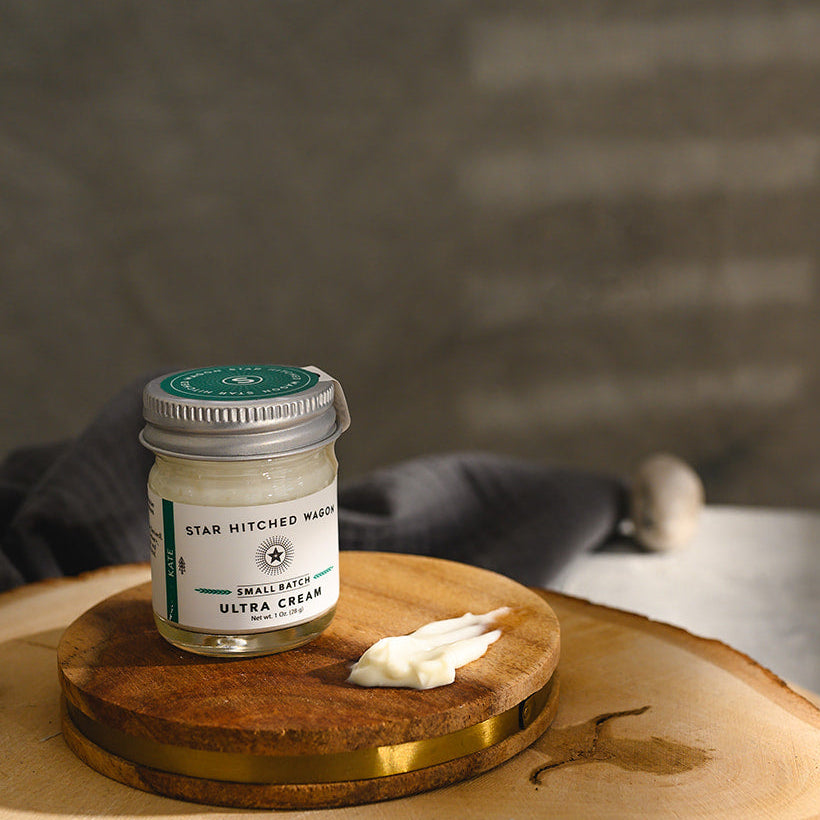 A small glass jar of Star Hitched Wagon Kate Ultra Cream sits on a round wooden slice, with a dollop of ultra cream next to jar.