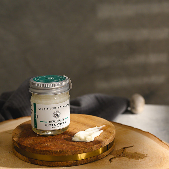 A small glass jar of Star Hitched Wagon Kate Ultra Cream sits on a round wooden slice, with a dollop of ultra cream next to jar.