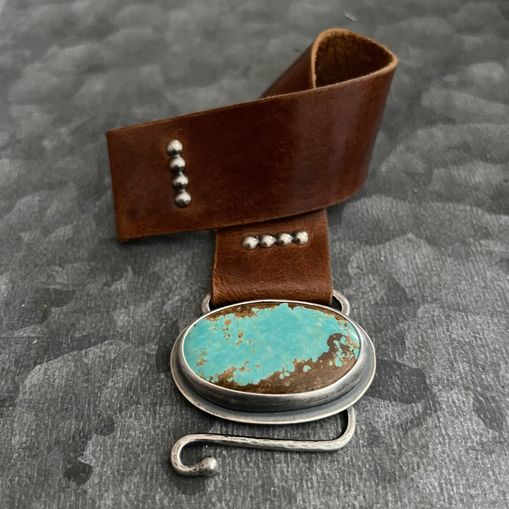 Leather Bracelet with Turquoise featuring a #8 turquoise stone set in sterling silver, brown leather band with silver rivets, and a handcrafted hook closure.