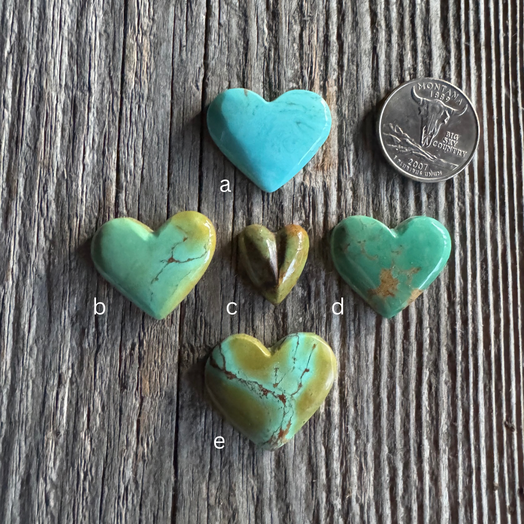 5 turquoise heart stone choices on weathered wood surface.