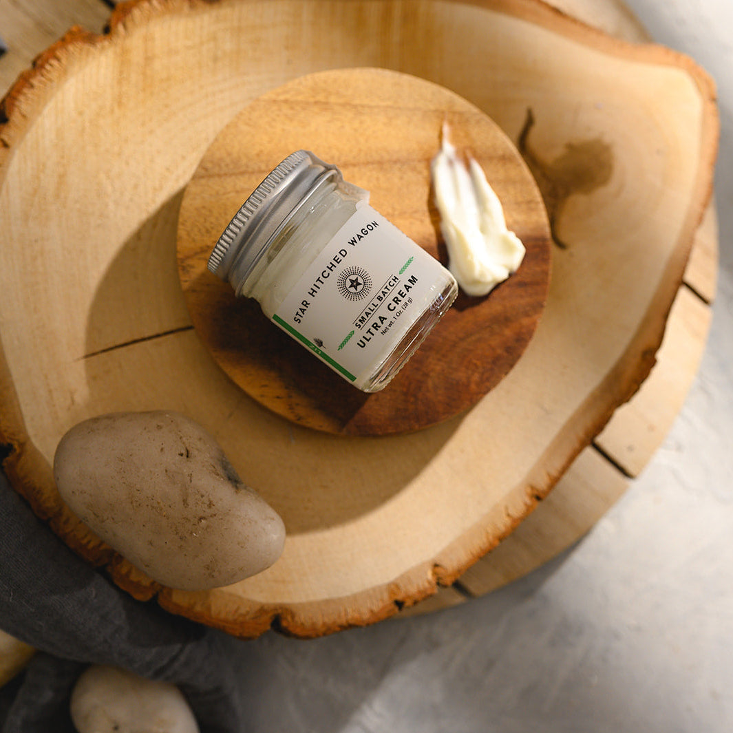 A small glass jar of Star Hitched Wagon Liz Ultra Cream lays on a round wooden slice, with a dollop of ultra cream next to jar.